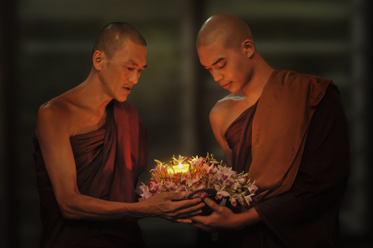 Two monks holding a candle surrounded by flowers, symbolizing spirituality and tradition.