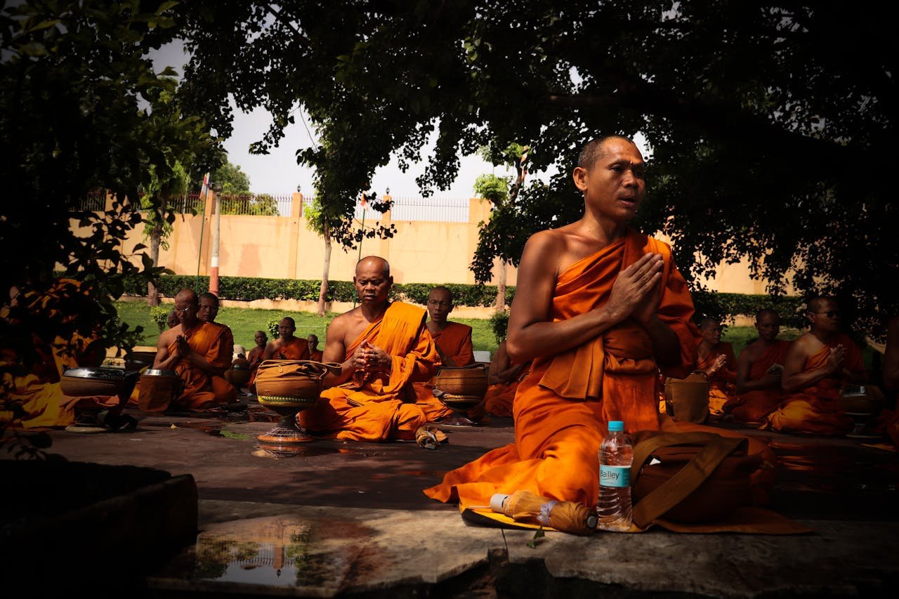 Group of monks meditating outdoors in traditional orange robes, focused in deep contemplation.