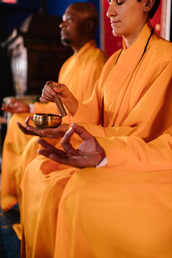 Buddhist monks in saffron robes meditate with prayer bowls in a temple.